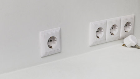 Four electrical sockets on a light wall and one electrical plug with a wire. A white electrical plug...