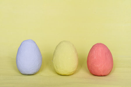 Light blue, light yellow and dark pink handmade eggs on a pastel yellow background. Easter concept....
