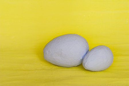 Two decorative eggs of different sizes painted with gray paint on a yellow background. Easter concept.の写真素材