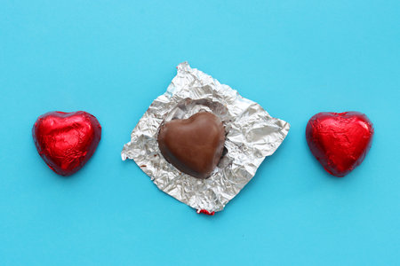 Two chocolates and one with an unwrapped wrapper.Three chocolate hearts on a blue background, top...