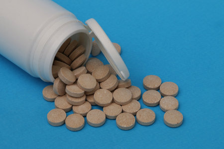 White plastic bottle with scattered brown pills on a blue paper background. Medicine and health concept.の写真素材