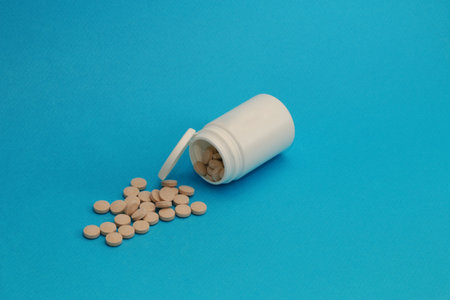 Medicine and health concept. Close up of tablet pills spilling from Plastic pill bottle on blue background with selective focus.の写真素材