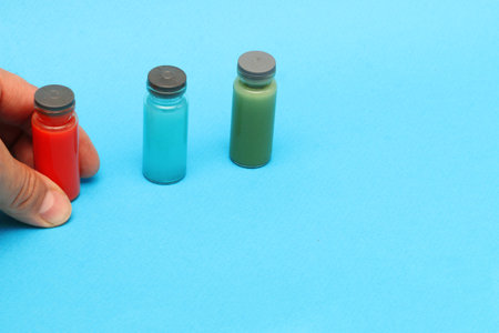 A man's hand holds a bottle with a blood test, blue and green bottles with chemical reagents on a blue background.....の写真素材