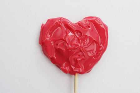 Red heart-shaped lollipop on a stick, on a white background. Gift for Valentine's Day.