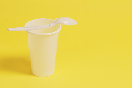 A white plastic glass and a spoon inserted into it on a yellow background.の写真素材