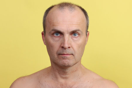 A man 45-55 years old with a hairy chest on a yellow background.