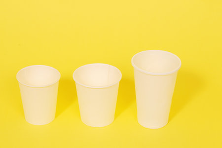 Three white plastic disposable cups on a yellow paper background.の写真素材