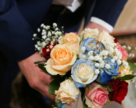The grooms hands hold the brides bouquet with red, blue, pink roses, top view.の写真素材