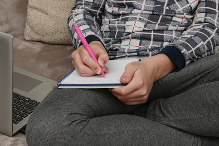 The boy writes out in the notebook the necessary information for self-education. Distant remote video education.の写真素材