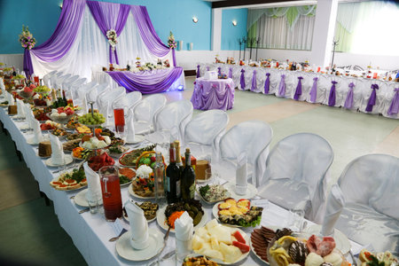 The interior of a large restaurant with wedding decor from curtains, bouquets of flowers, tables with a white tablecloth, a lot of beautiful and varied food on the tables.の写真素材