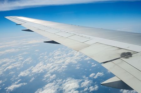Airplane wing in the blue sky with white clouds