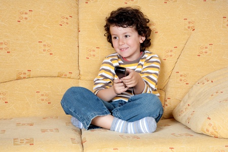 Beautiful child with the remote control of television sitting on the couchの写真素材