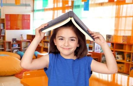 Brunette little girl with a book on her head in the classの写真素材