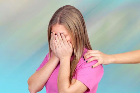 Sad teenager covering her face and a hand offering help isolated over a blue backgroundの写真素材