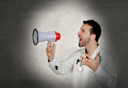 Doctor shouting whit a megaphone on a gray and irregular backgroundの写真素材