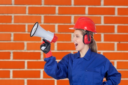 Industrial worker woman with a megaphone with a brick wall of bacgroundの写真素材