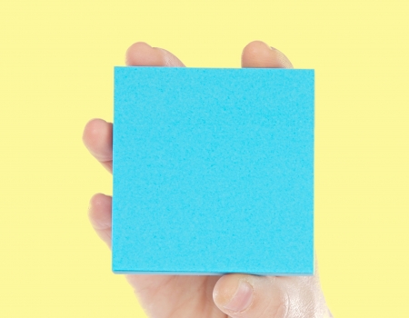 Hand holding a blue paper for notes on a yellow backgroudnの写真素材