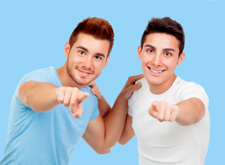 Couple of best friends pointing to the camera on a blue backgroundの写真素材