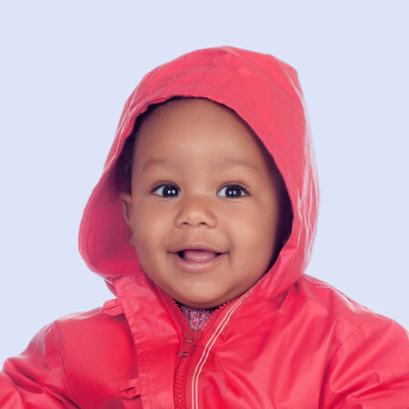 Adorable african baby with a beautiful smile and a red raincoat on a blue backgroundの写真素材