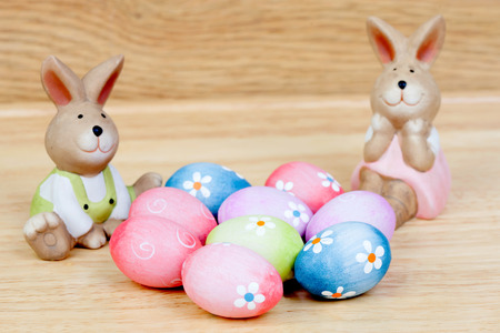 Funny rabbits ceramic with Easter eggs decorated with daisies on wooden background