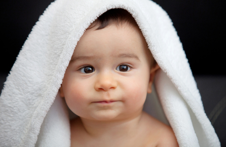 Cute baby covered with white blanket and black eyesの写真素材