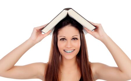 Attractive student woman with brackets an a book on the head isolated on a white backgroundの写真素材