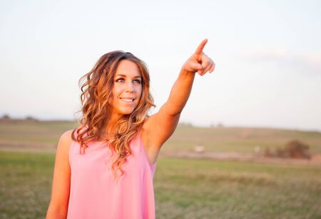 Beautiful young woman indicating something in the countryside with beautiful lightの写真素材