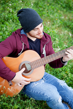 Cool handsome guy with beard playing guitar at outsideの写真素材