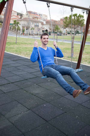 Young cool man sitting on a swing in the parkの写真素材