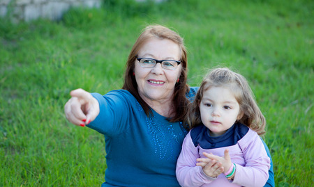 Proud grandmother with her granddaughter sitting on the grass in the fieldの写真素材