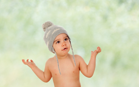 Adorable baby with wool cap asking somenthing with green background