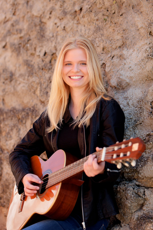 Cool blonde girl playing guitar leaning against a stone wallの写真素材
