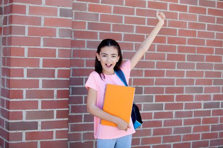 Preteenager girl next to a red brick wall with the backpack and books
