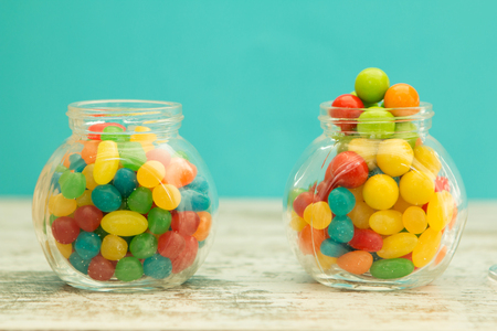 Three glass jars full of jellybeans on wooden table with blue background