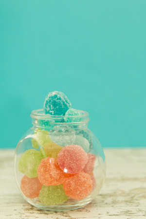 Glass jar full of jelly beans on a wooden table with blue backgroundの写真素材