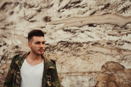 Attractive guy with jacket military stylish on a wall of mud of backgroundの写真素材