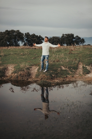 Attractive guy with jeans and white jersey next to a river in the meadowの写真素材