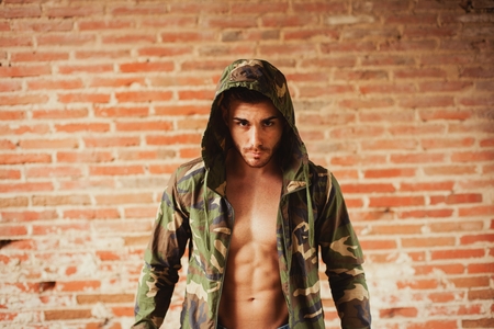 Attractive man showing his abs under a camouflage jacketの写真素材