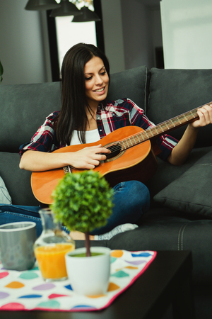 Brunette woman at home in the morning playing the guitarの写真素材