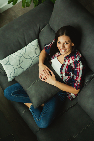 Cool brunette girl sitting on the sofa at homeの写真素材