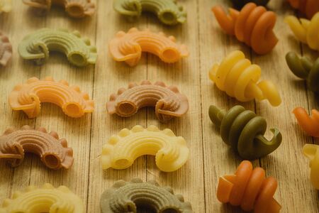 Colorful pasta with nice shapes lined up on wooden boardの写真素材