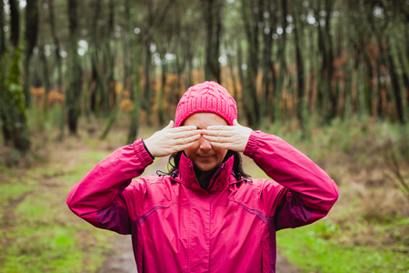 Woman with pink wool hat in the forest covering her eyesの写真素材