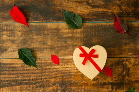 Present with heart shape green and red leaves on a wooden backgroundの写真素材