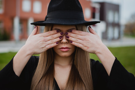 Pretty stylish girl with a hat covering her face with the hands