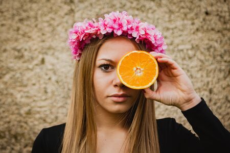 Beautiful portrait of a blonde girl with a pink flower and a wreath of orangeの写真素材