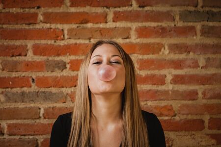 Funny girl making a pomp with a bubble gum and a brick wall of backgroundの写真素材