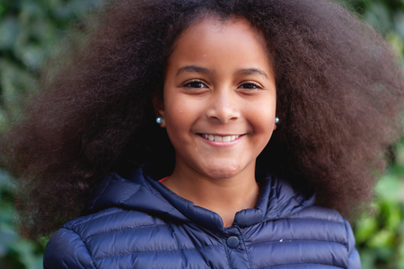 Pretty girl with long afro hair in the garden with a blue coatの写真素材
