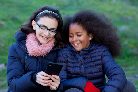 Two girls looking at the mobile in the park.