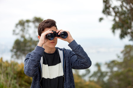 Teenager guy looking with binoculars in the natureの写真素材