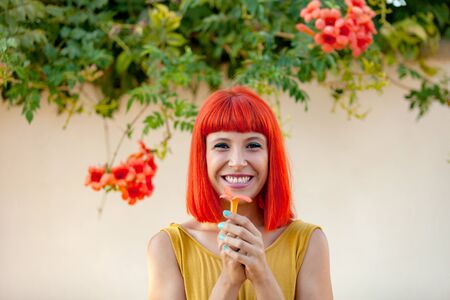 Happy woman with red hair and yellow dress near to a plant with beautiful flowersの写真素材